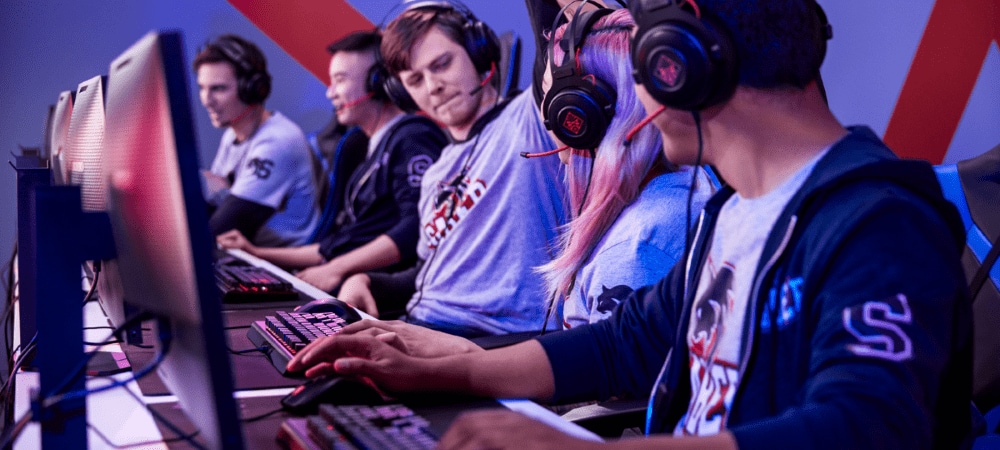 A team of esports players wearing matching jerseys and headsets compete at computers while two member raise their hands to high-five in celebration